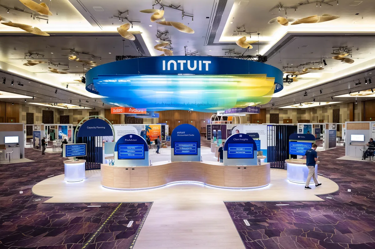 Expo hall with a suspended Intuit ring sign above product demos