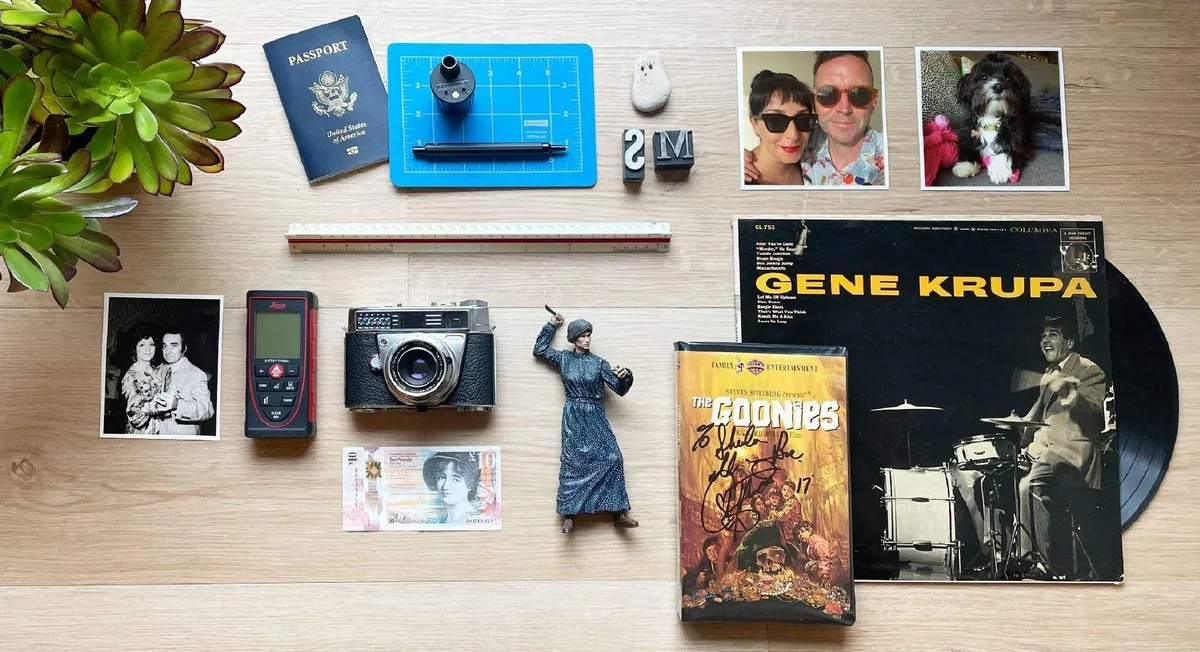 Flat lay of a passport, architect&rsquo;s scale, vintage camera, laser measure, family photos and a Gene Krupa record